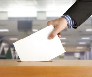 Hand putting a voting ballot in a slot of box